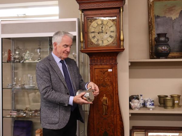 man looking at an antique in front of antique tall standing clock